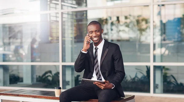 Geschäftsmann lächelt mit Handy auf Stadtbank — Stockfoto