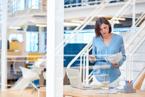 Empresária olhando para a papelada no escritório moderno — Fotografia de Stock