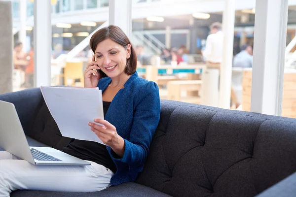 Zakenvrouw praten op telefoon tijdens het kijken naar papierwerk — Stockfoto