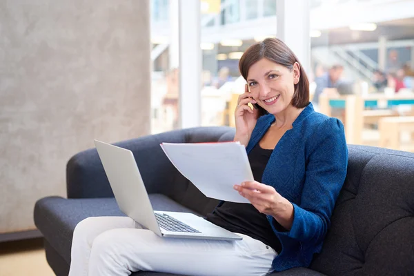 Empresária falando ao telefone enquanto olha para a papelada — Fotografia de Stock