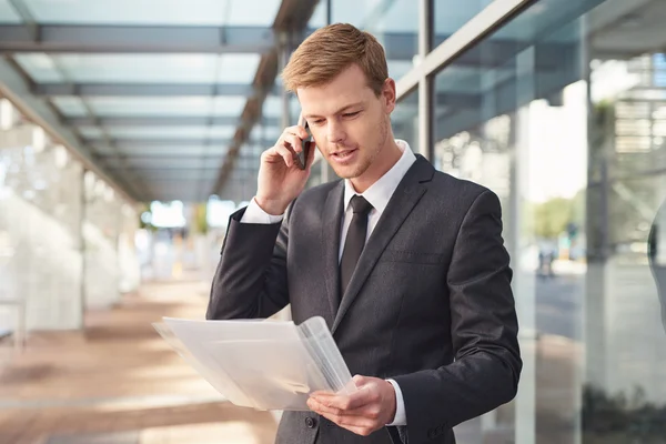 Hombre de negocios hablando por celular y leyendo papeleo —  Fotos de Stock