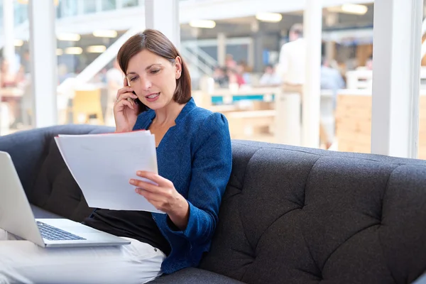 Empresária falando ao telefone enquanto olha para a papelada — Fotografia de Stock