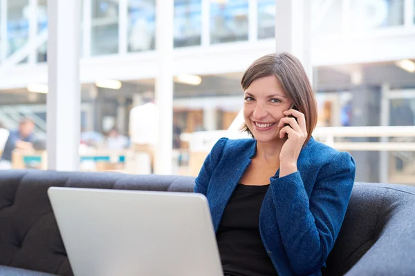 Empresária usando telefone no sofá com laptop — Fotografia de Stock