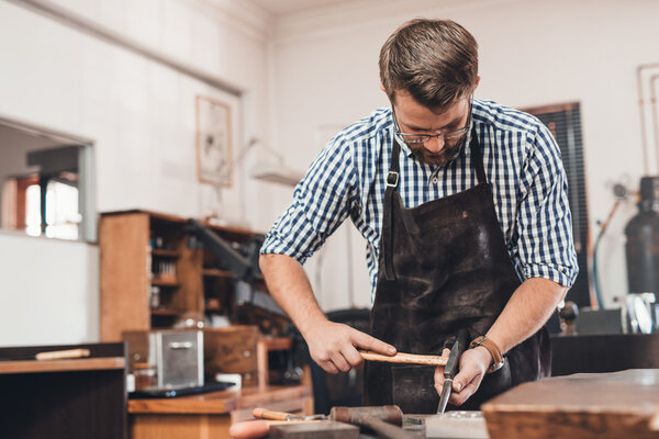 ювелир с помощью молотка и манделя для формирования кольца
