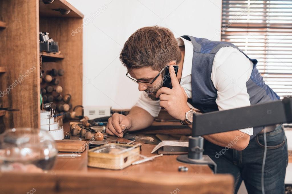 jeweler examining ring and talking on cellphone