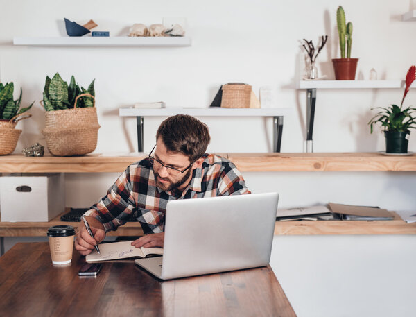 entrepreneur writing in notebook next to laptop