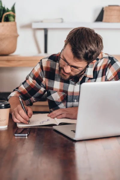 Ondernemer schrijven in notitieblok naast laptop — Stockfoto