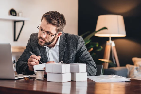 Empresario escribiendo direcciones en paquetes para la entrega — Foto de Stock