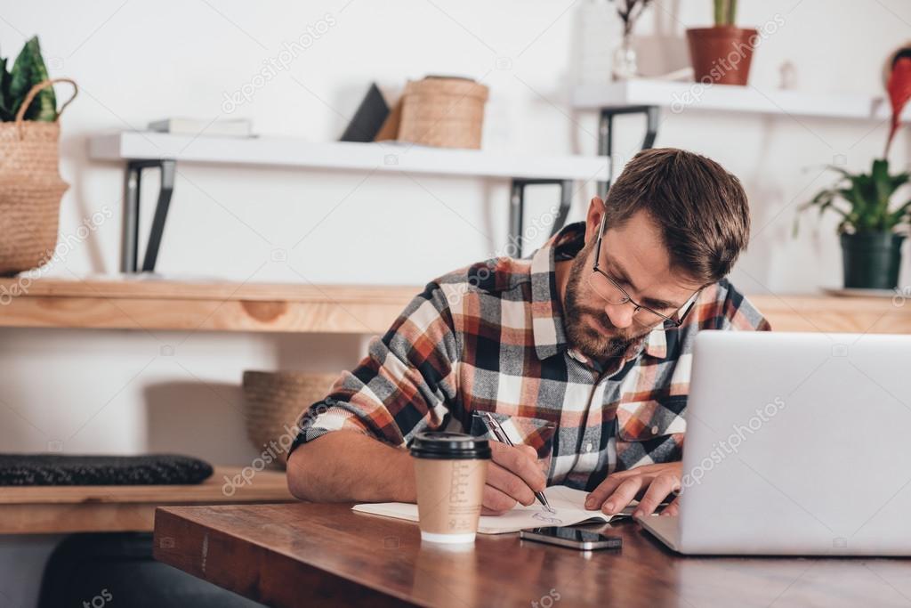 entrepreneur writing in notebook next to laptop