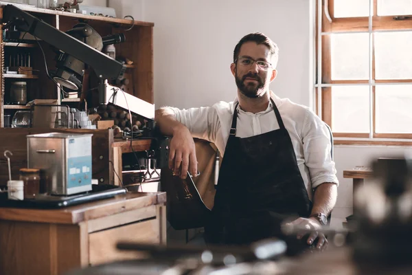 Jeweler sitting in workshop full of tools — Stock Photo, Image