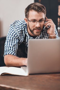 Telefonda konuşmak ve dizüstü bilgisayarda çalışan kuyumcu