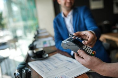 Bir kafede müşterinin parasını akıllı bir telefonla almak için terminali kullanan bir garsona yakın çekim.
