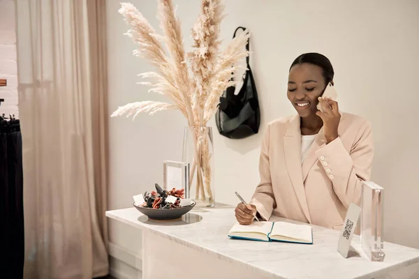 Jovem Empreendedora Afro Americana Sorridente Falando Telefone Escrevendo Notas Balcão — Fotografia de Stock