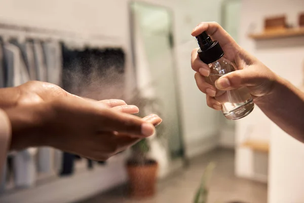 Closeup of an African American female customer having sanitizer sprayed on her hands before entering a clothing boutique