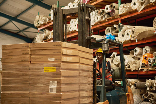 Молодая африканская оператор вилочных погрузчиков перевозит коробки по полу текстильного склада