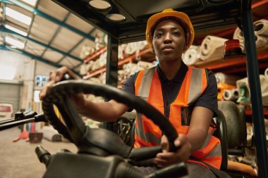 Genç Afrikalı kadın forklift operatörü bir tekstil deposunda kutu taşıyor.