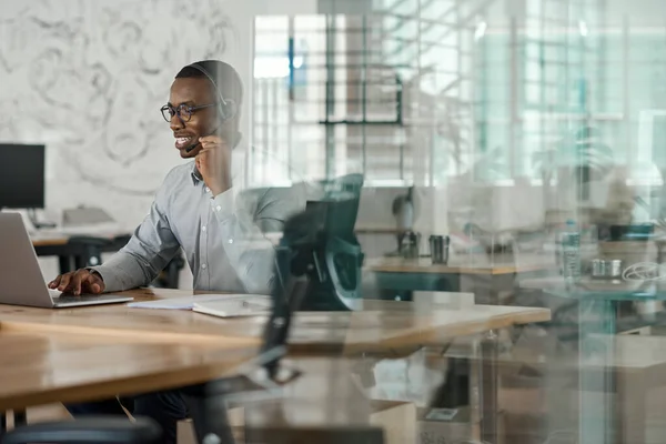 Jovem Empresário Africano Sorridente Trabalhando Laptop Conversando Fone Ouvido Enquanto — Fotografia de Stock