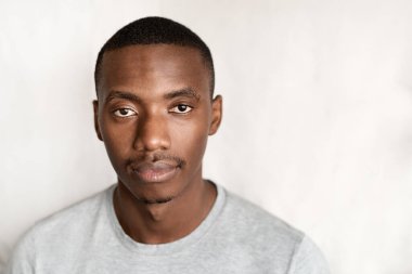 Evde duvarın önünde duran kendinden emin, tişörtlü genç bir Afrikalı adamın portresi.