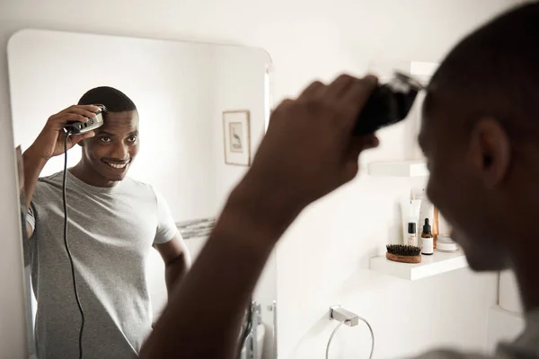 笑着站在浴室镜子前的非洲年轻人用电锯修剪头发 — 图库照片
