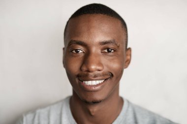 Evde duvarın önünde dikilmiş gülümseyen genç bir Afrikalı 'nın portresi.