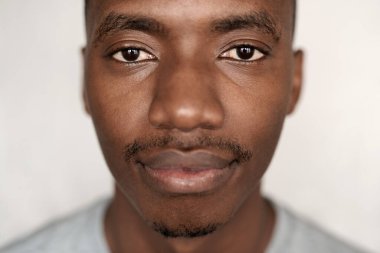 Evinde duvarın önünde duran kendine güvenen, tişörtlü Afrikalı genç bir adamın yakın portresi.