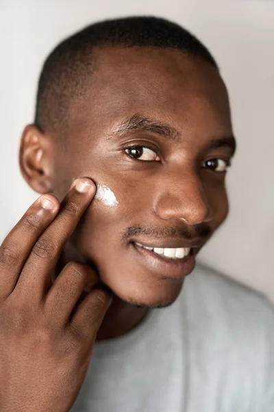 一个面带微笑的年轻非洲男子在脸上涂了乳白色润肤霜 — 图库照片