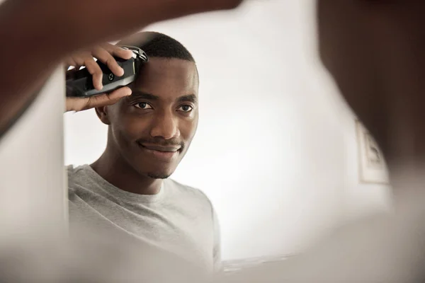 站在浴室镜子前 笑着用电钳剪头发的非洲年轻人 — 图库照片