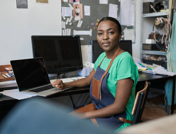 Portrait of a young African female artisan using a laptop while working at a desk in her studio