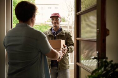 Afrikalı kurye evinin önünde duran müşteriye paketleri teslim ederken gülümsüyor.