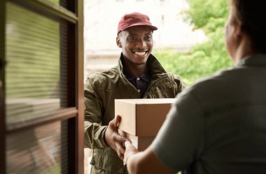 Afrikalı kurye, apartmanının ön kapısının önünde duran bir müşteriye bazı paketleri teslim ederken gülümsüyor.