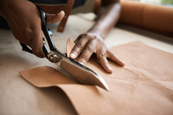 Closeup of a African female artisan cutting a piece of leather with shears at a bench in her workshop