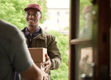 Gülümseyen Afrikalı kurye apartmanının kapısının önünde duran müşteriye paket teslim ediyor.