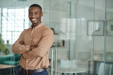 Modern bir ofiste kollarını kavuşturmuş gülümseyen genç bir Afrikalı iş adamının portresi.