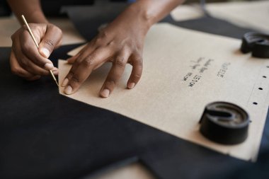Afrikalı bir kadın zanaatkarın stüdyosundaki bankta çalışırken deri üzerinde bir desen kullanması.