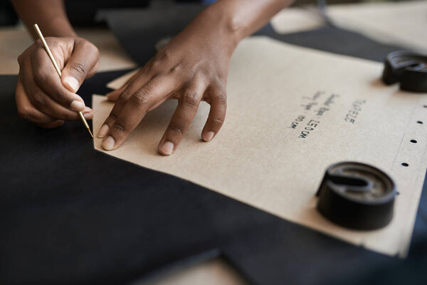 Closeup of an African female artisan using a pattern on a piece of leather while working at a bench in her studio