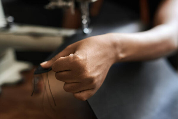 Closeup of an African female artisan working on a piece of leather with a sewing machine in her studio