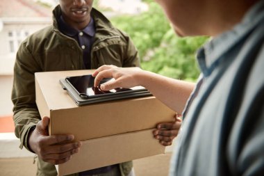 Bir Afrikalı kuryenin, bir apartmanın ön kapısında durup tablete dijital imza atması.