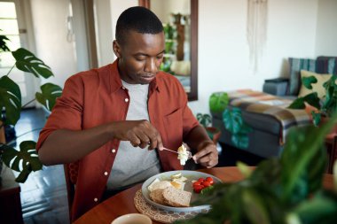 Genç Afrikalı adam yemek masasında otururken sağlıklı ev yapımı yumurta kahvaltısının tadını çıkarıyor.