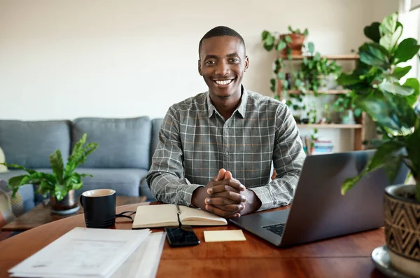 一个微笑的非洲商人用笔记本电脑在客厅的桌子边远程工作的画像 — 图库照片