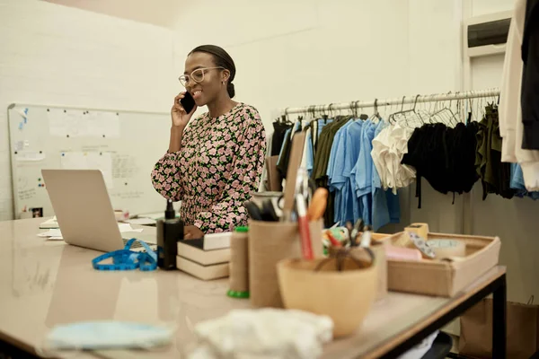 Uśmiechnięta Młoda Afrykańska Projektantka Mody Rozmawiająca Przez Telefon Komórkowy Sprawdzająca — Zdjęcie stockowe