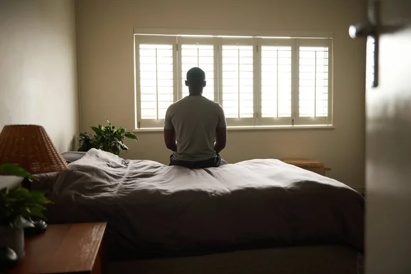 一个年轻的非洲男人坐在床边的后视镜出现在他的家里 从窗户往外看 — 图库照片
