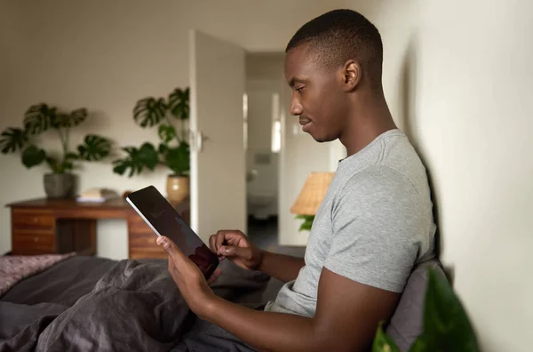 아프리카 남자가 아침에 집에서 침대에 디지털 태블릿으로 인터넷을 둘러보고 있습니다 — 스톡 사진