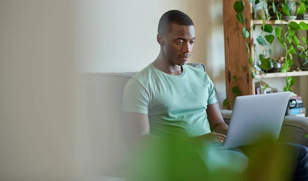 非洲年轻人坐在客厅沙发上 一边上网一边用笔记本电脑干活 — 图库照片