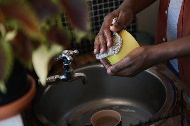 Genç Afrikalı bir adamın mutfağındaki lavaboda bulaşık yıkarken dairesinin etrafında çalışması.