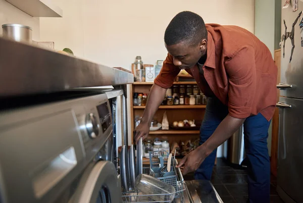 非洲年轻人在家里的厨房里把盘子堆放在洗碗机里做家务活 — 图库照片