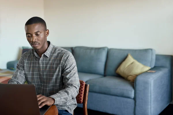 年轻的非洲商人在自家客厅的桌子边远程工作时使用笔记本电脑 — 图库照片