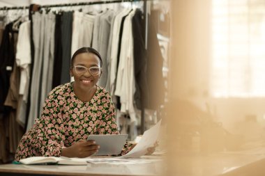 Üretim stüdyosunda dijital tablet üzerinde çalışan gülümseyen Afrikalı bir moda tasarımcısının portresi