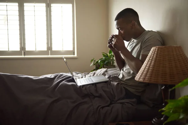 Jovem Africano Sentado Cama Manhã Navegando Internet Com Laptop Bebendo — Fotografia de Stock