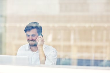dizüstü bilgisayarda çalışan ve telefonda konuşurken işadamı
