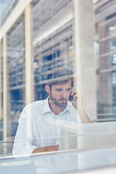 Empresário trabalhando no laptop e falando no telefone — Fotografia de Stock